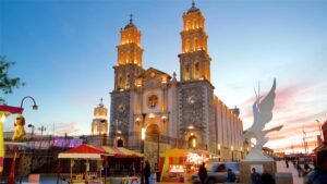 Catedral iluminada con puestos callejeros y escultura al atardecer.