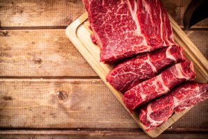 Carne roja cruda marmoleada cortada en trozos sobre tabla de madera.