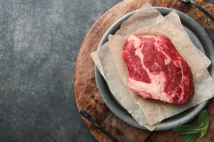Raw beef steak. Raw fresh Chuck roll steak with rosemary, salt and pepper on cutting board on dark concrete background. Raw b