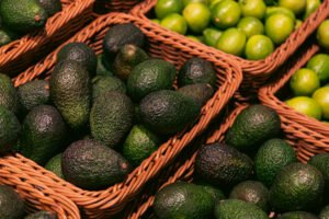 Canastas de mimbre con aguacates verdes y limas al fondo.