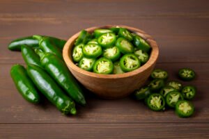 Chiles jalapeños verdes, enteros y en rodajas, en cuenco de madera.