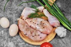 Raw chicken fillet and legs on wooden plate with fresh vegetables