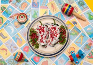 Chiles en nogada sobre cartas de Lotería y juguetes mexicanos.
