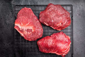 Tres piezas de carne de res cruda sobre una rejilla negra.